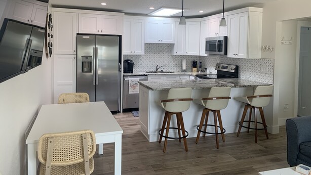 Una cocina moderna con armarios blancos, electrodomésticos de acero inoxidable, una encimera de mármol y taburetes de bar.