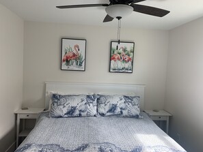 A bedroom with a bed, two nightstands, a ceiling fan, and two framed paintings of flamingos.
