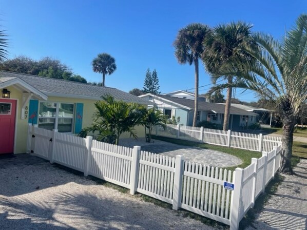 A row of single-story cabins with white picket fences, surrounded by palm trees and a clear blue sky.