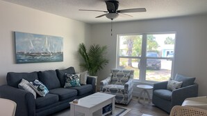 Una sala de estar moderna con un sofá gris, un sillón estampado, una mesa de centro blanca y un ventanal con vistas al exterior.