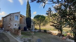 Une maison en pierre dotée d’un patio aménagé avec des meubles d’extérieur et un grand arbre.