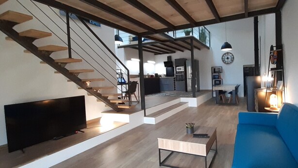 Un salon moderne doté d’un téléviseur à écran plat, d’un canapé bleu, d’une table basse en bois et d’un escalier menant à un niveau supérieur.
