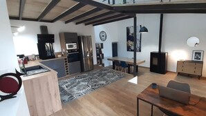 Une cuisine moderne équipée d’un four à micro-ondes, d’un réfrigérateur et de meubles de rangement en bois. On y trouve également un coin repas avec une table et des chaises, ainsi qu’un salon avec un canapé et une lampe.