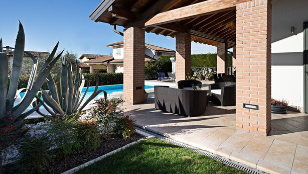 Un patio techado con mobiliario exterior, una piscina y un jardín con plantas de agave.