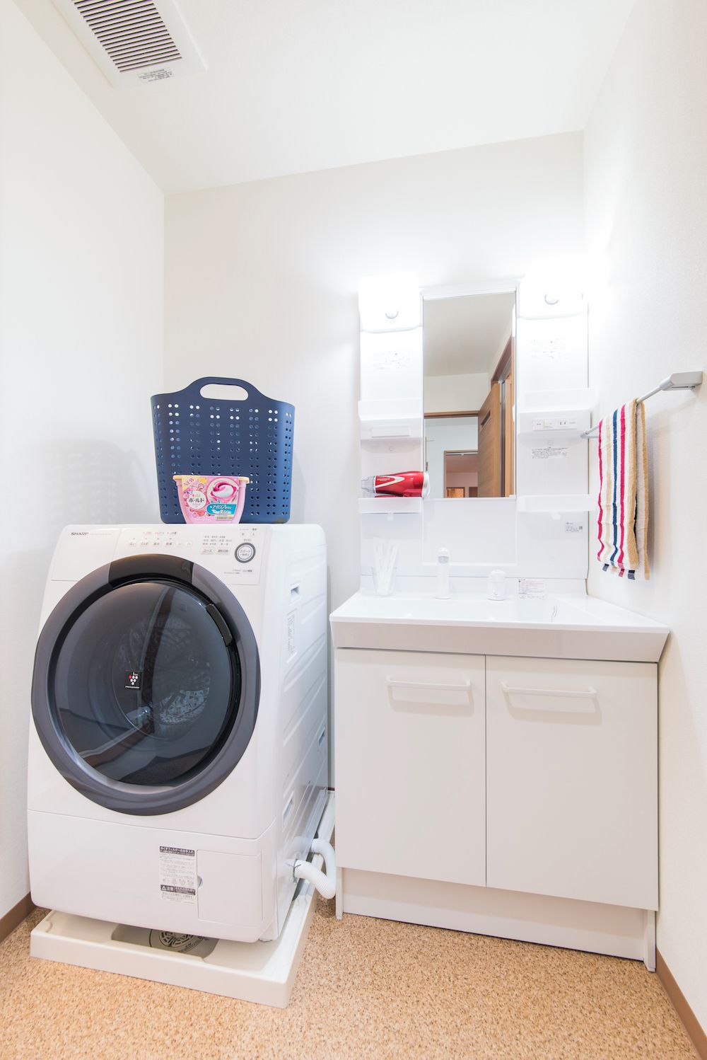 A compact laundry area with a front-loading washer and dryer, a white sink with a mirror above, and a towel rack on the wall.