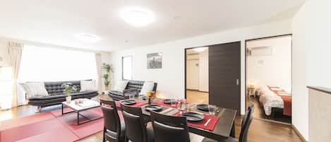 Un salon moderne avec un canapé, une table à manger et des chaises. Une porte coulissante donne accès à une chambre.