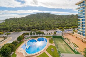 A swimming pool with a heart-shaped design, surrounded by a landscaped area with a tennis court and a building with balconies.