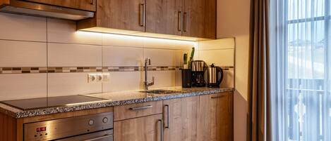 A kitchen with wooden cabinets, a stainless steel range, a built-in oven, a sink, and a window with curtains.