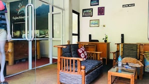 Una sala acogedora con un sofá de madera, una mesita y una silla. Hay una puerta de cristal que da a un pasillo con un espejo y un cartel en la pared.
