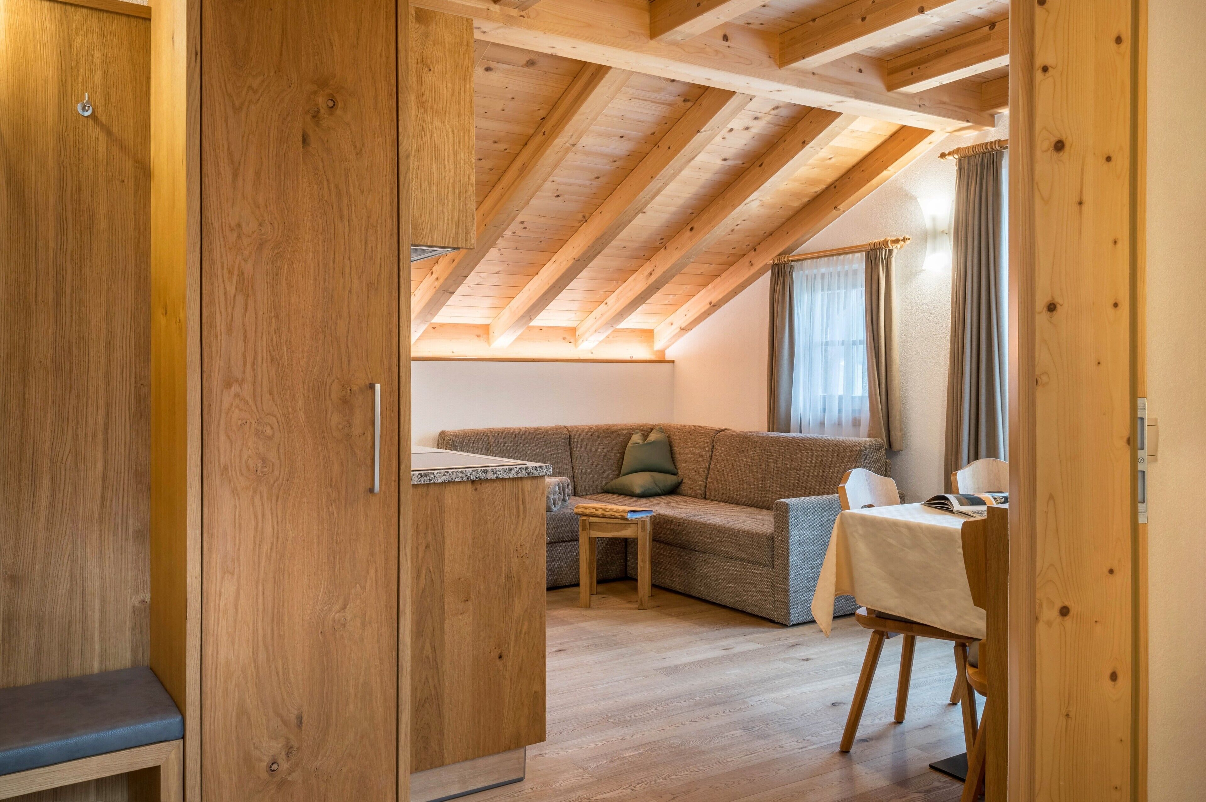 A wooden interior with a loft bedroom, a sofa, a small table, and a dining area.