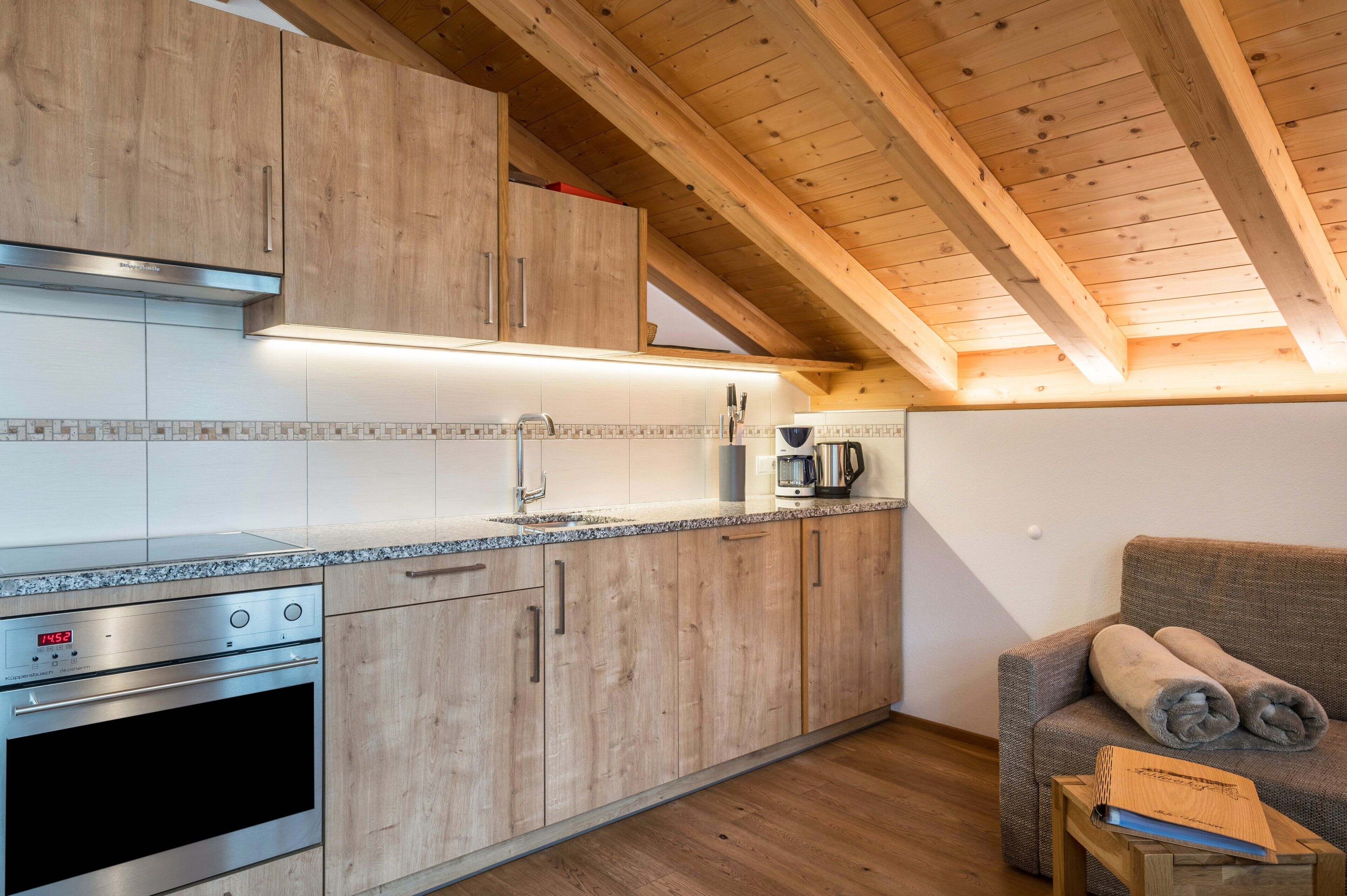Moderni keittiö, jossa on puiset kaapit, sisäänrakennettu uuni ja kahvinkeitin.