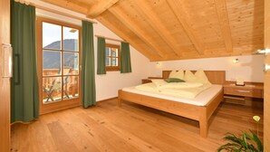Ein Schlafzimmer mit Holzboden, einem Bett, einem Nachttisch und Blick ins Freie.