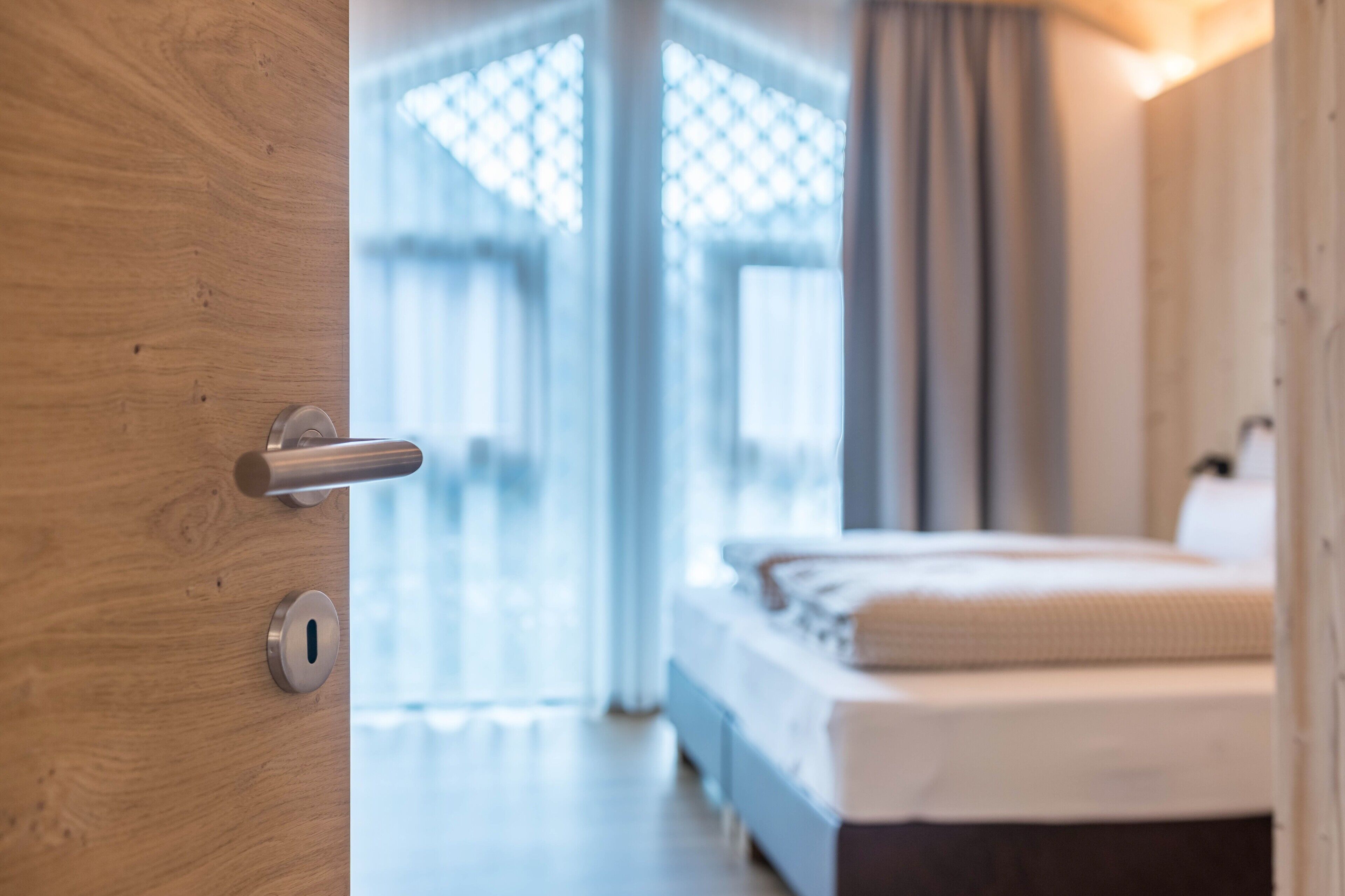 Een hotelkamer met een houten deur, een bed en uitzicht door een raam met gordijnen.