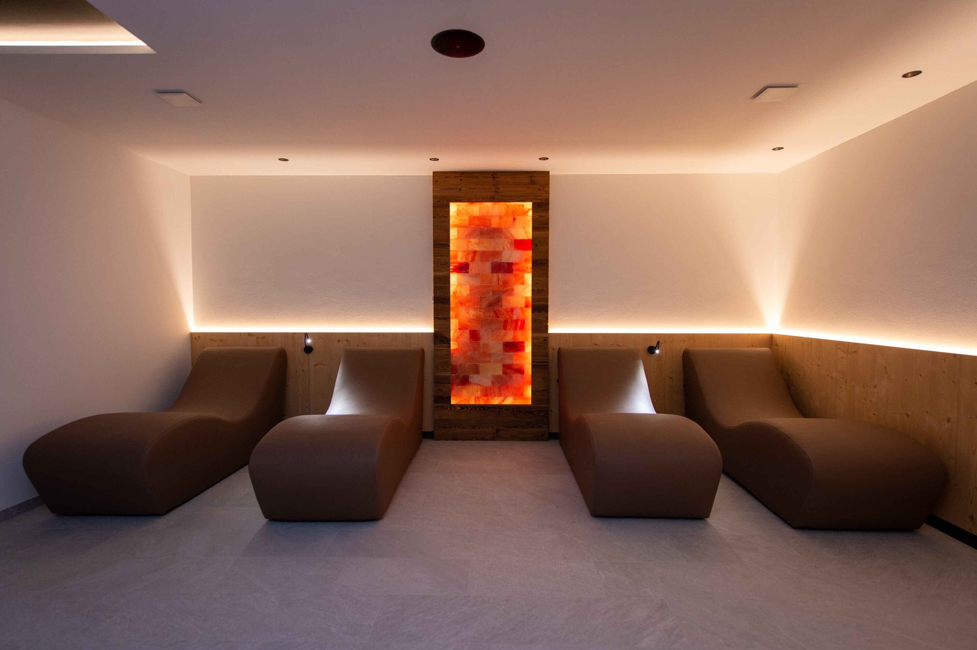 Een moderne spa-ruimte met twee comfortabele zithoeken, een houten accentmuur en inbouwverlichting.