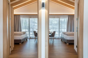 A mirrored room with two beds, a dining table, and large windows.