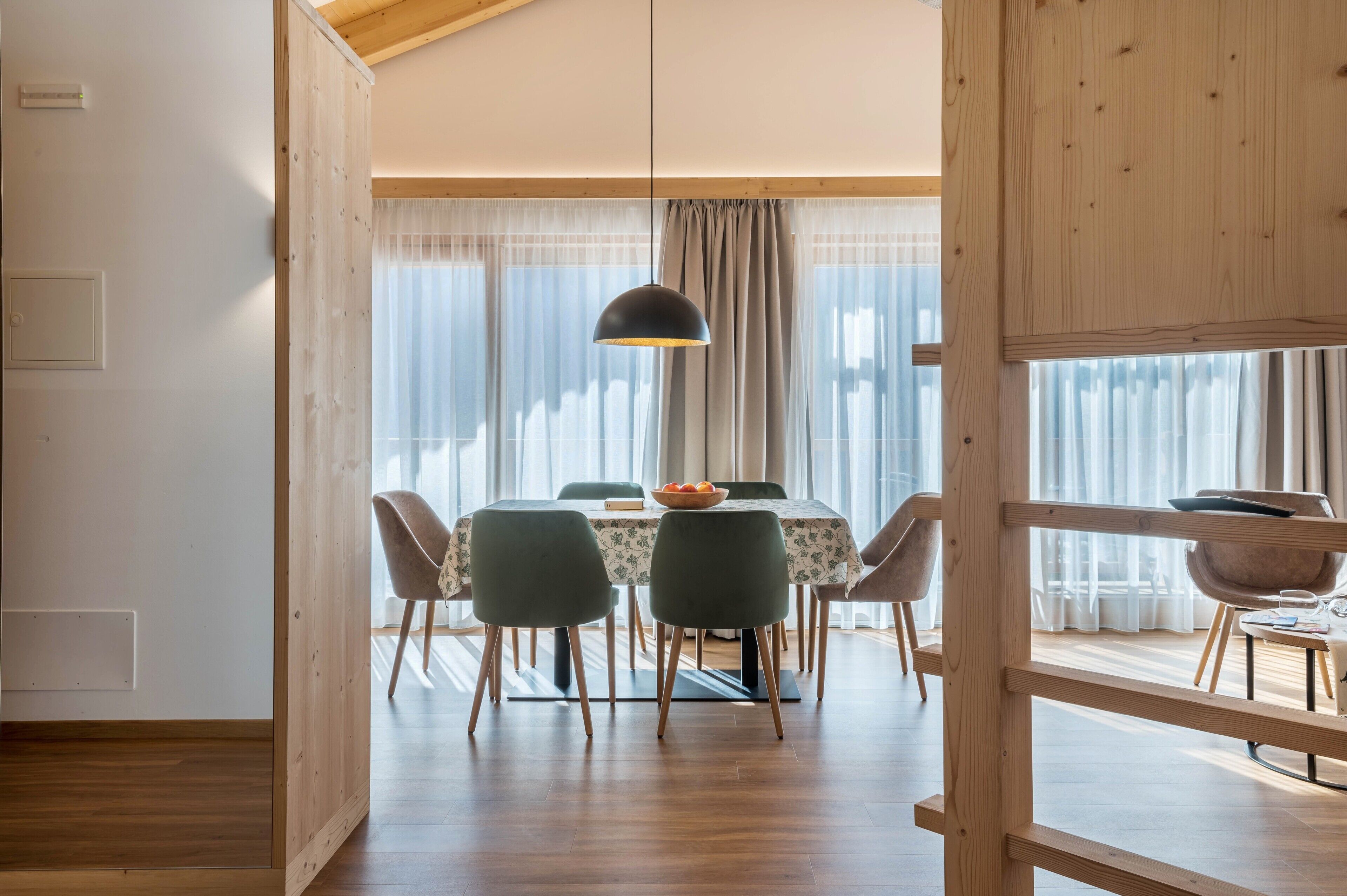 Spiseområde med et bord, stole, en pendel og udsigt gennem et vindue med gardiner.