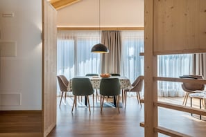 Spiseområde med et bord, stole, en pendel og udsigt gennem et vindue med gardiner.