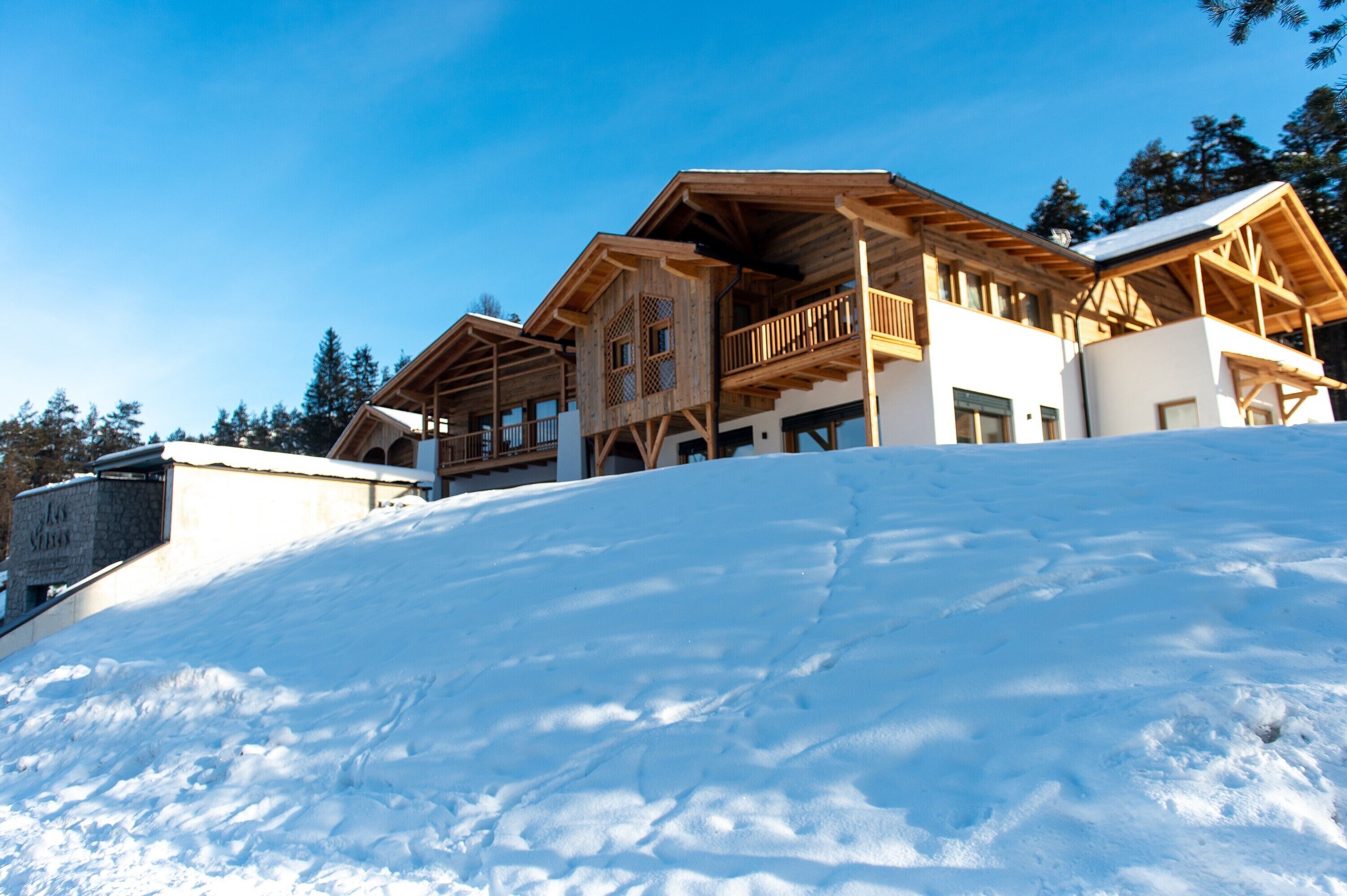 A wooden chalet with multiple balconies and large windows, situated on a snowy slope.