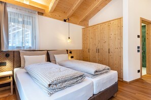 A room with two beds, wooden ceiling beams, a large window with sheer curtains, and a green-tiled door.