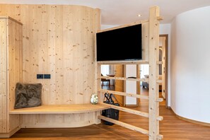 A wooden interior with a bench, a TV mounted on a wooden structure, and a small table with a flower vase.