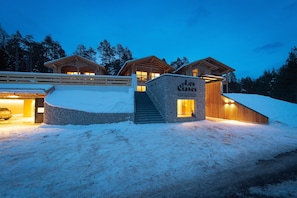 Una cabaña con entrada de piedra, cabañas de madera y un paisaje cubierto de nieve.
