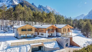 A chalet-style hotel with multiple wooden structures, a stone entrance, and a snowy mountain backdrop.