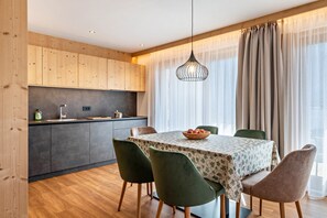 A modern kitchen with wooden cabinets, a dining table with a floral tablecloth, and green chairs.
