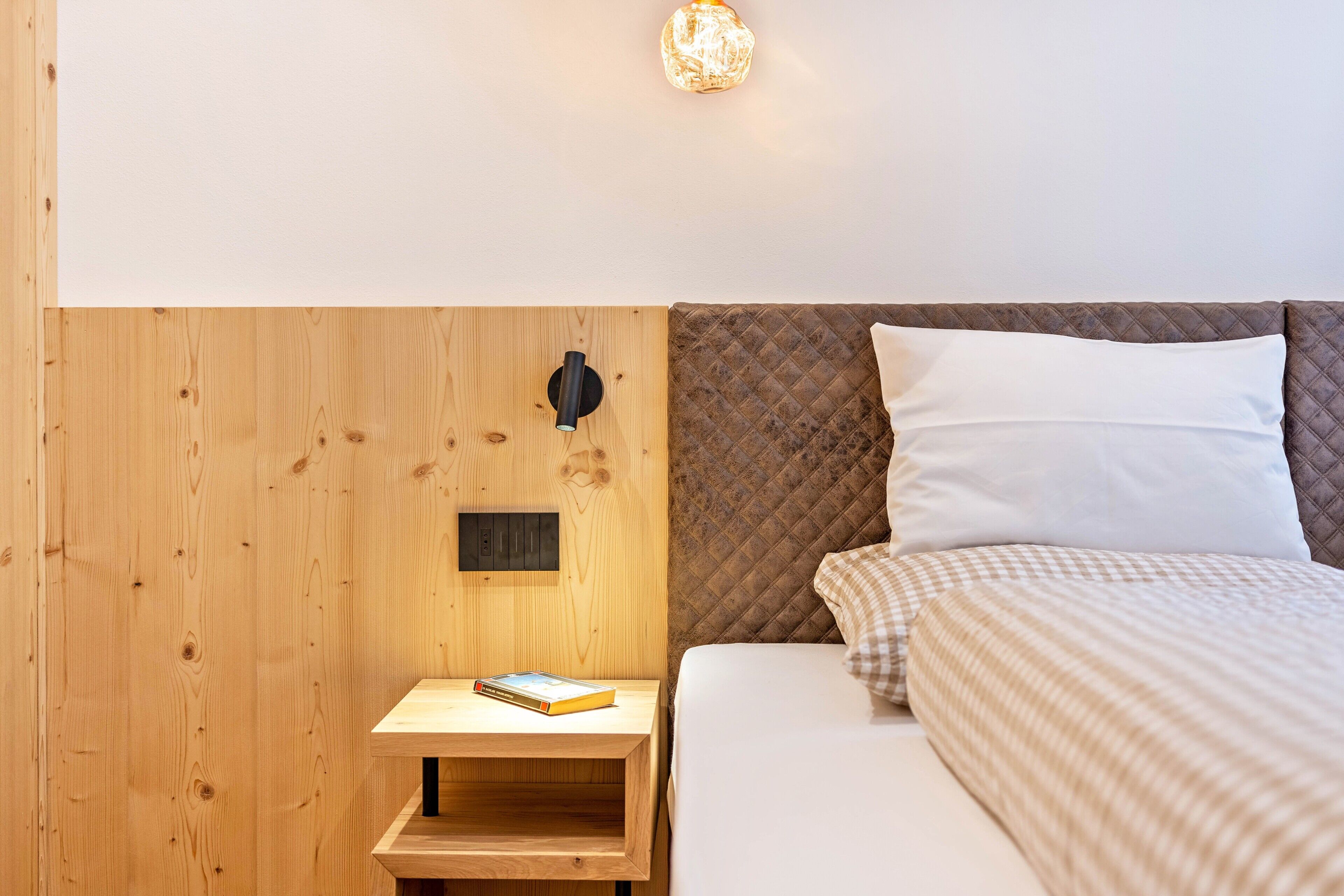 Una parete in legno con un comodino, un letto con testata imbottita e un punto luce a parete.