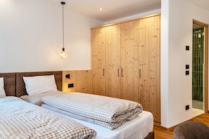 Une chambre avec deux lits, une armoire en bois, un luminaire suspendu et une porte recouverte de carreaux verts.