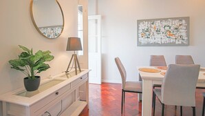 A dining area with a table, chairs, a potted plant, a mirror, and a painting on the wall.