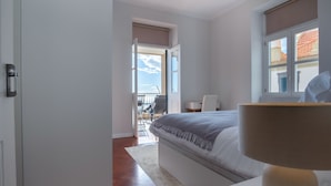 A bedroom with a bed, a bedside lamp, a window, and a view of the outside.