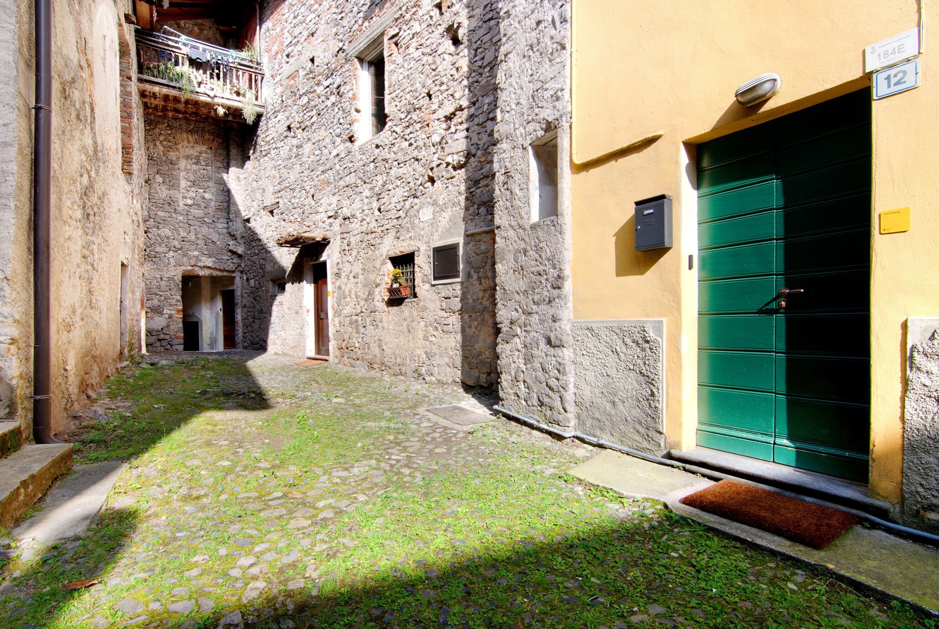 A narrow cobblestone alley with a stone building on one side and a yellow building with a green door on the other.