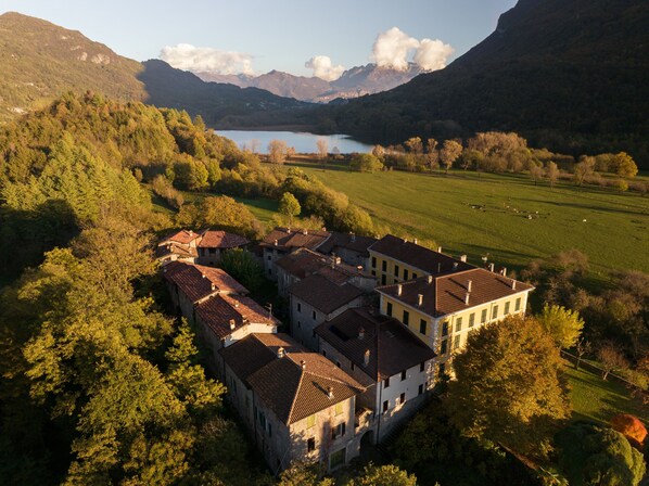 Un complejo arquitectónico tradicional con varias construcciones, rodeado de exuberante vegetación y un lago, con montañas al fondo.