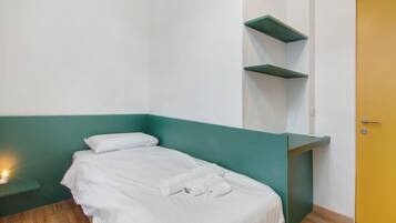 Ein Einzelbett mit weißer Bettwäsche, eine Wand in Grünton, ein Holzboden und eine gelbe Tür.