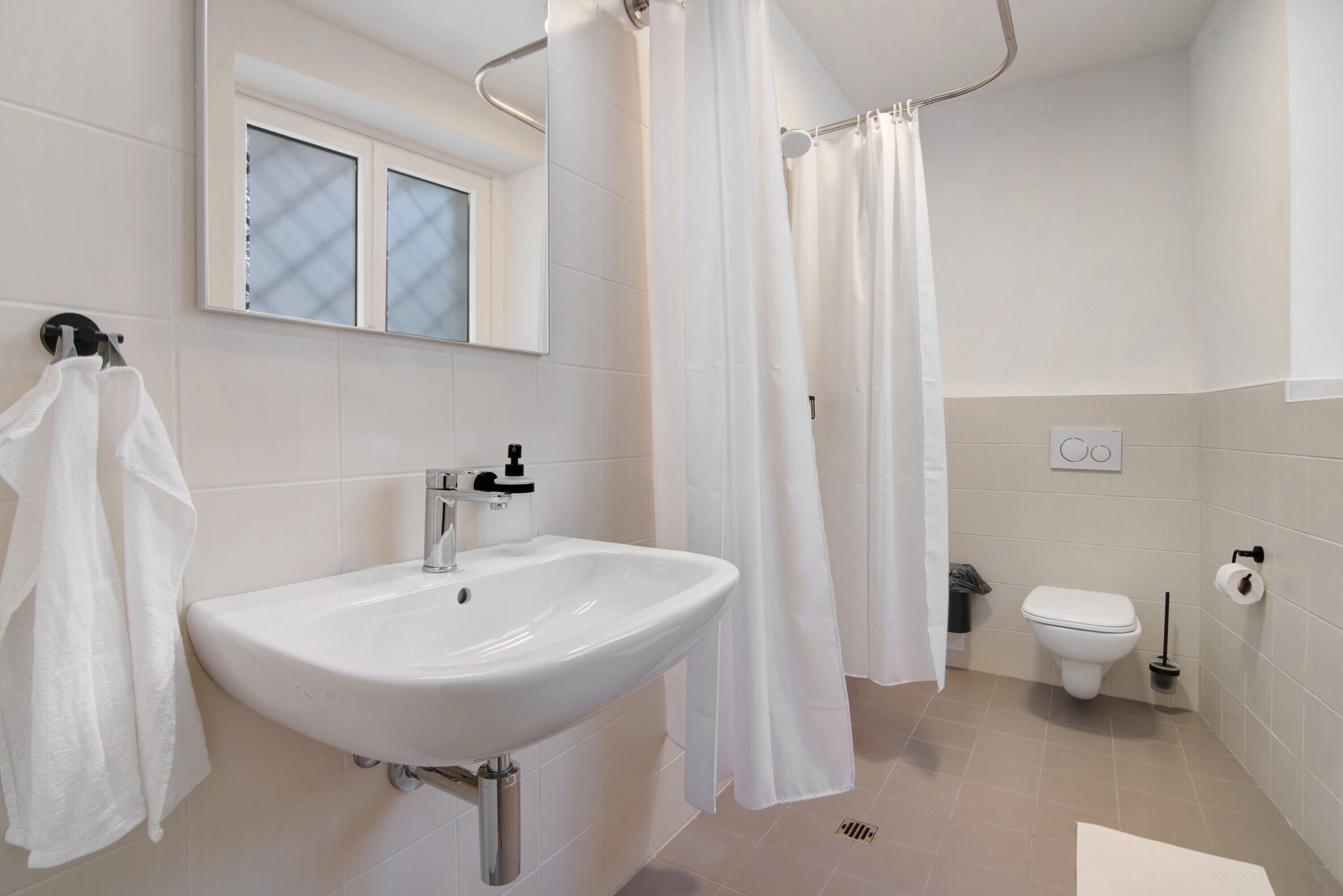 Een badkamer met een witte wastafel, toilet, douchegordijn en een raam met geëtste glas.