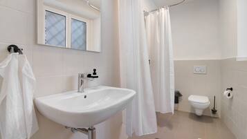 Een badkamer met een witte wastafel, toilet, douchegordijn en een raam met geëtste glas.