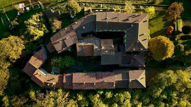 En bild tagen från luften som visar ett modernt hus med en unik takdesign, omgivet av frodig grönska och en välskött gräsmatta.