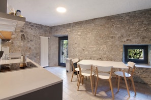 Una cocina moderna con pared de piedra, una zona de comedor con mesa y sillas blancas, y un ventanal con vistas.