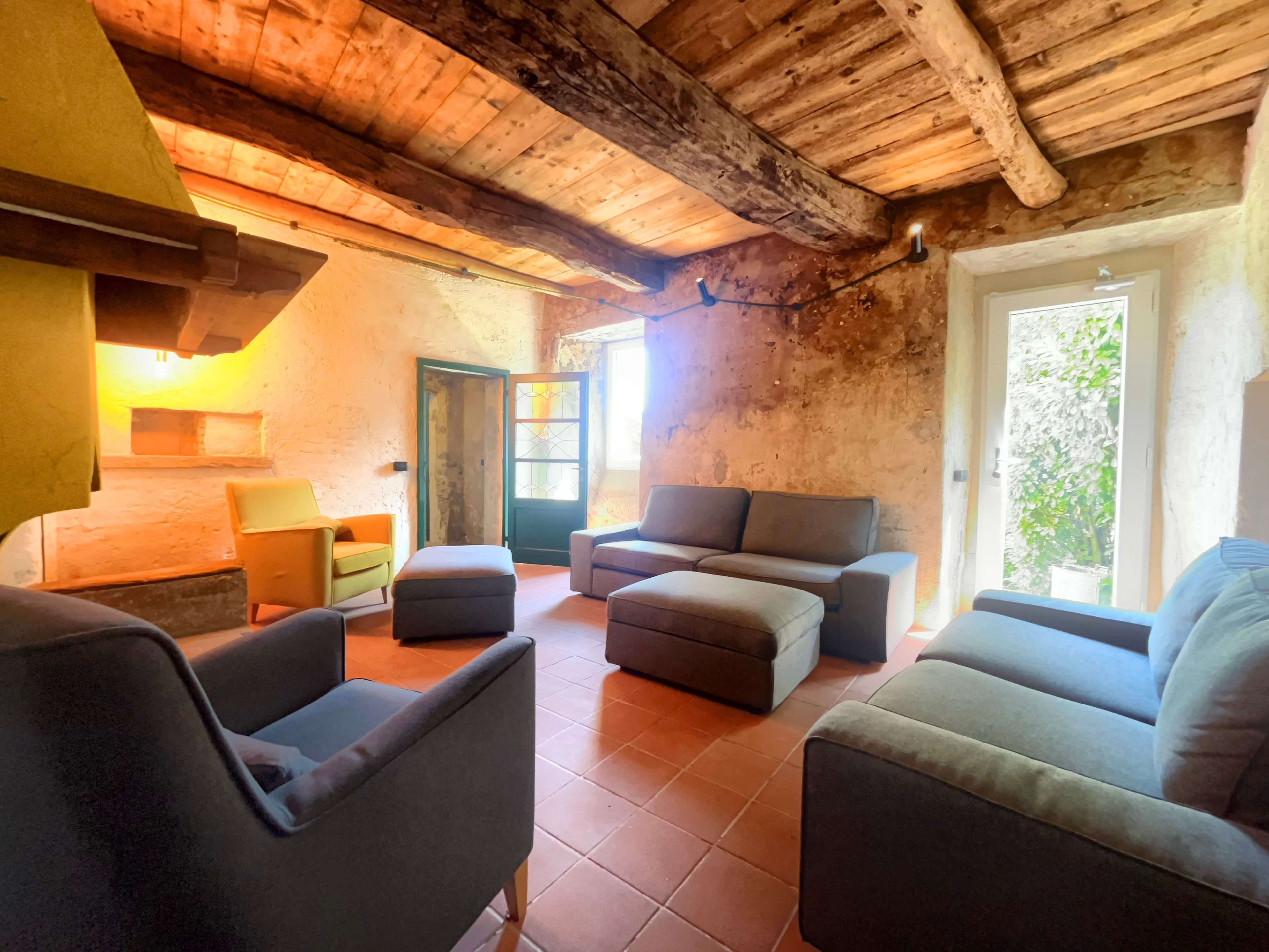 Un intérieur rustique avec un haut plafond en bois, une cheminée et un coin salon comprenant des canapés et des fauteuils.