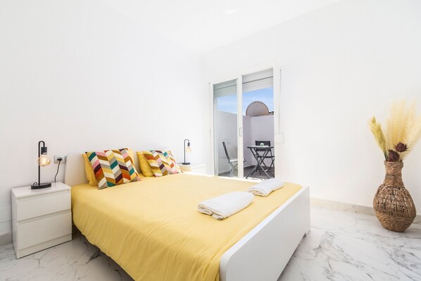 A bedroom with a bed, bedside table, lamp, and a vase with pampas grass.