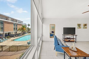 A modern living room with a large window overlooking a pool and a building with balconies.