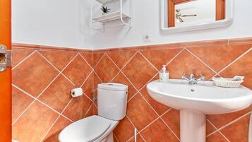 A bathroom with a toilet, sink, and a shelf with toiletries.