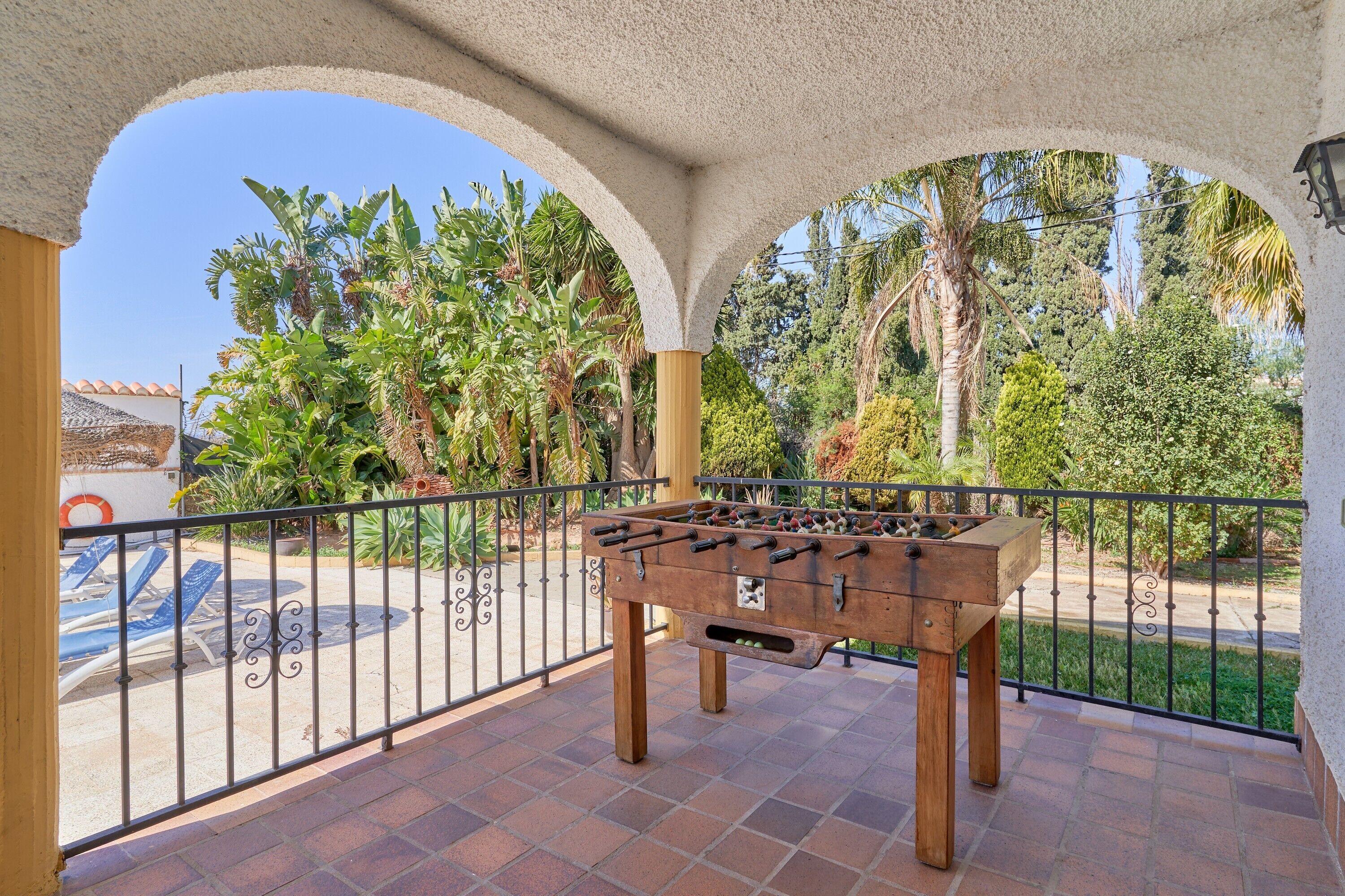 A foosball table on a balcony with a view of palm trees and a pool.