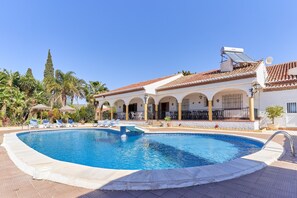 A swimming pool with lounge chairs, a covered patio, and a building with arches and a tiled roof. - Holiday Home 'Cabrera' with Sea View, Private Pool and Wi-Fi (Puntalon)