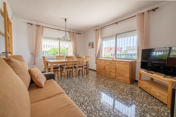 A living room with a sofa, dining table, chairs, a TV, and a wooden cabinet.