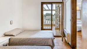 A bedroom with two beds, a wooden door, and a view of the outside. - Villa 'Olivera' with Private Terrace and Private Garden (L'Escala)