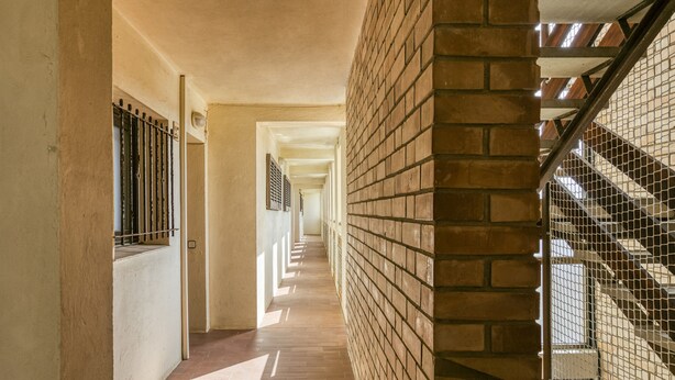 A corridor with a brick wall, a metal staircase, and a series of doors along the length.