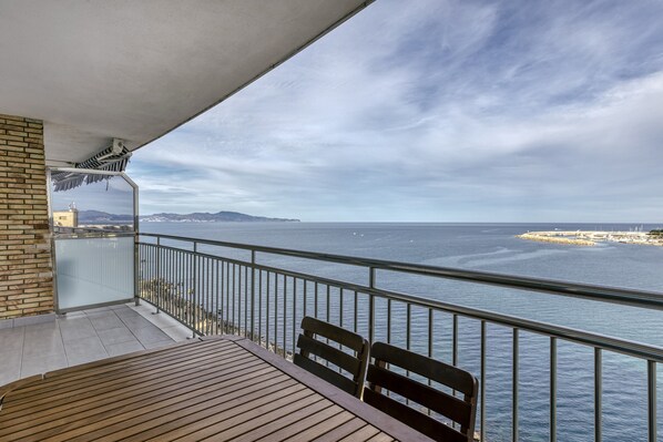 A balcony with a view of the sea, a wooden table, and two chairs. - Apartment 'Marinada' with Sea View, Shared Pool and Wi-Fi (l'escala)