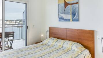 Un dormitorio con cama, cabecera de madera, un cuadro y balcón con vistas a edificios.