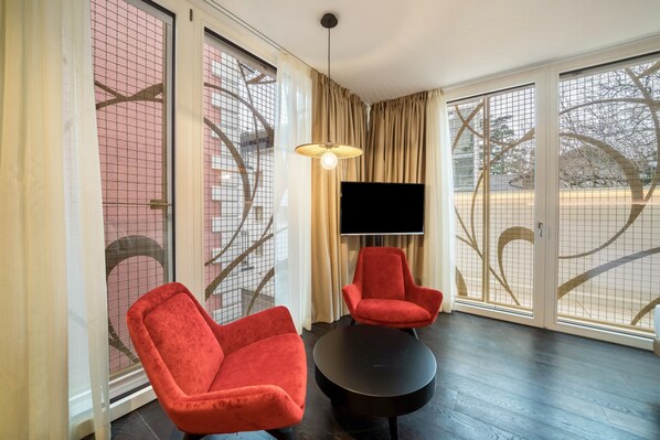 A room with two red chairs, a black table, a TV, and large windows with a view of trees and a building. - Villa Steiner 5 - Suzuka- Studio with balcony, air conditioning and wifi (Merano)